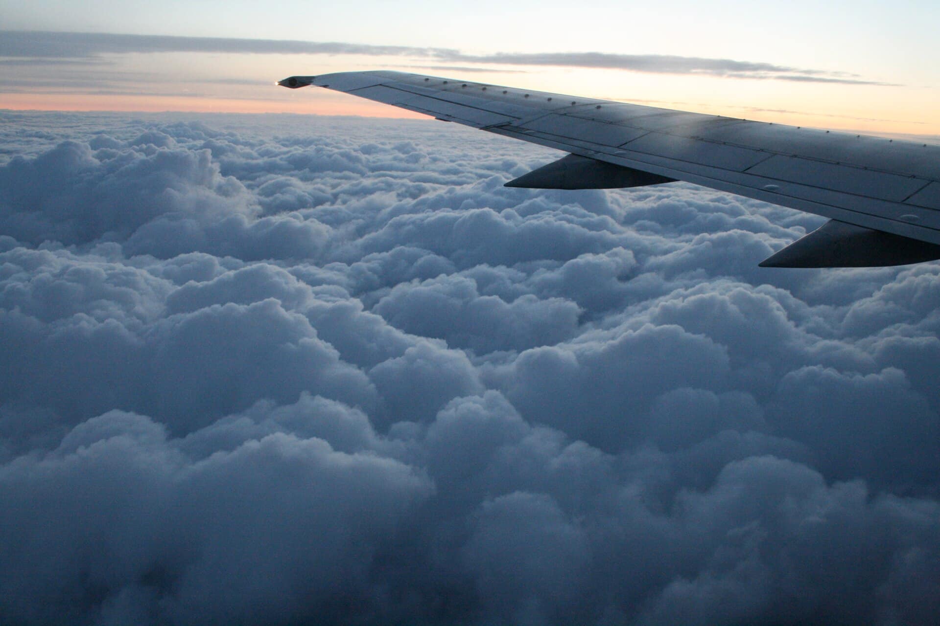Asa de avião sobre um mar de nuvens ao entardecer